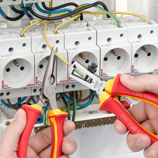 Facom E050408 insulated wire stripper and pliers used in electrical panel wiring, close-up photography.