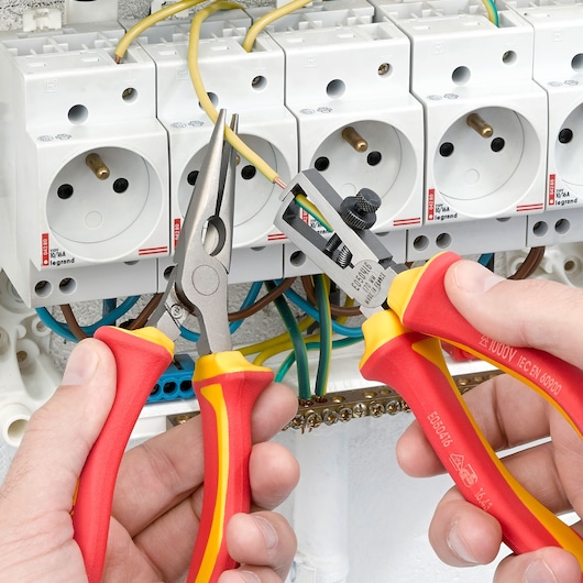 Facom E050408 insulated wire stripper and pliers used for electrical wiring in a power socket panel.