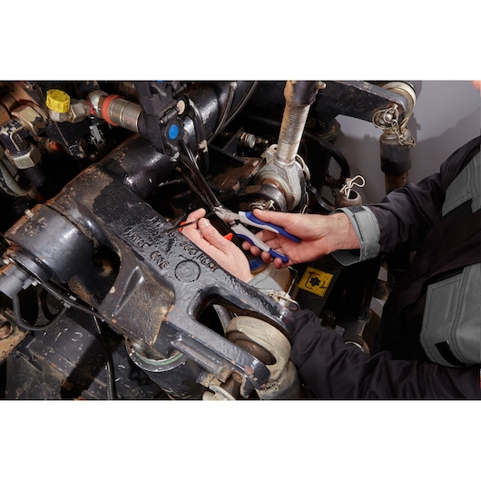 Facom E080209 pliers used to grip wire inside an industrial machine. Photo shows tool in technician's hand.