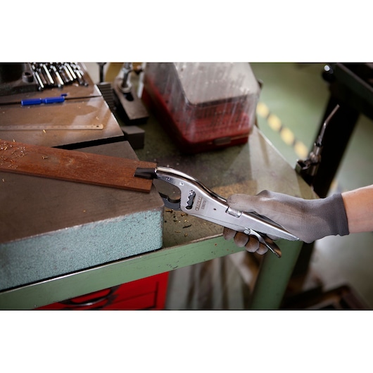 Facom E080701 locking pliers in use on a metal workpiece in a workshop with hand wearing grey glove.