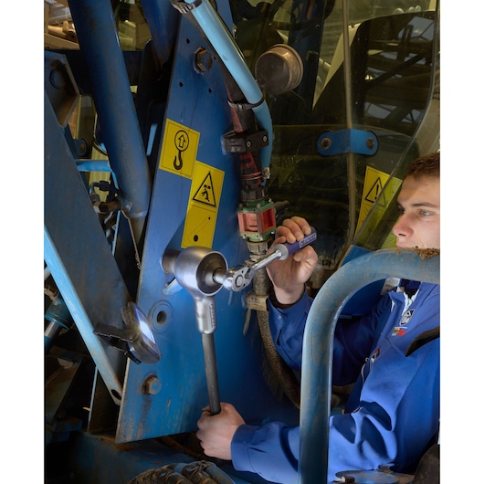 Photo of Facom E100103 ratchet wrench used by technician in blue coverall on industrial blue machinery.