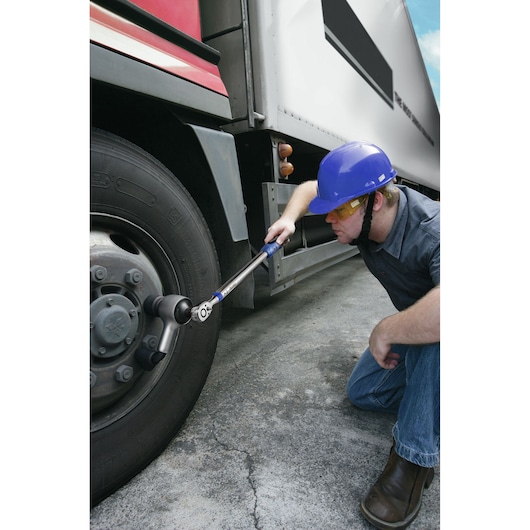 Facom E100105 torque wrench used by worker in blue helmet tightening truck wheel lug nuts outdoors.