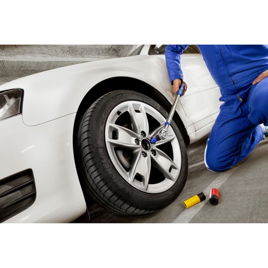 Facom E100108 torque wrench being used on a car wheel by a person in blue coveralls, sideways angle.