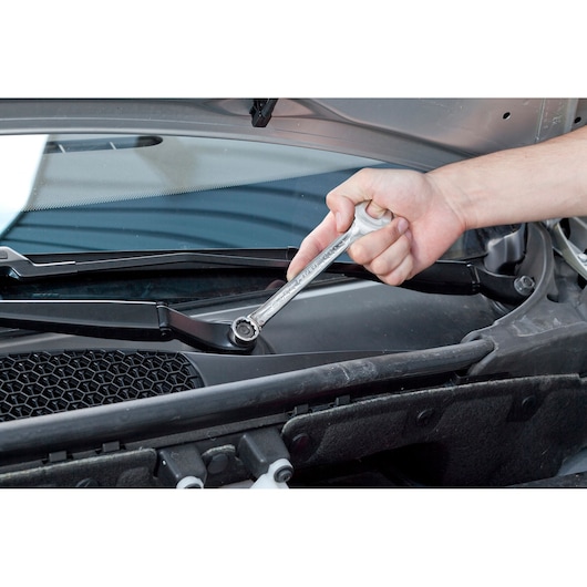 Facom E113235 ratcheting combination wrench used to tighten a bolt on a car windshield wiper assembly.