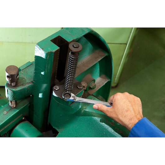 Facom ratcheting combination wrench E117372 used to tighten a bolt on industrial green machinery, side view.