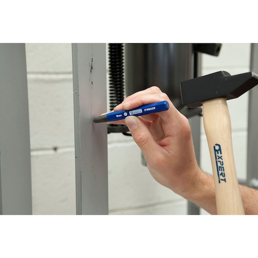 Photo of Facom E150501 metal chisel in use, held against gray metal with hammer for marking.