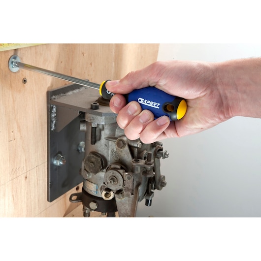 Facom E165206 screwdriver with blue and yellow handle, used to tighten a screw on wood near machinery.