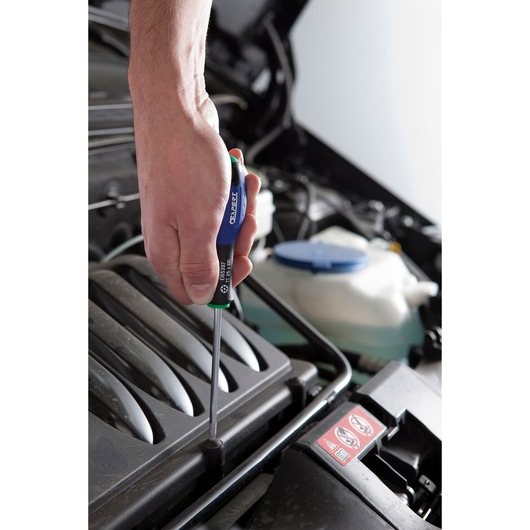 Photo of a hand using a Facom E165397 screwdriver with blue and green handle on a car engine.