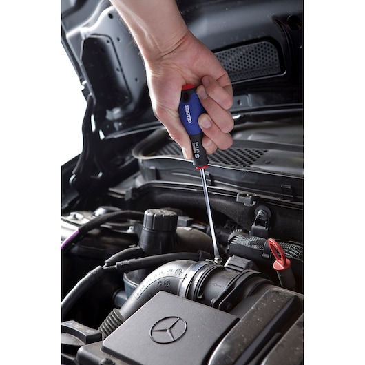 Facom screwdriver E165483 used on engine component, close-up photography showing hand grip.
