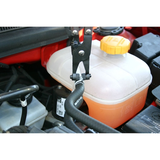 Facom E200501 hose clamp pliers used on a black hose near coolant reservoir in car engine bay.