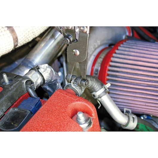 Facom E200504 pliers used on a hose clamp in an engine bay, close-up photography.