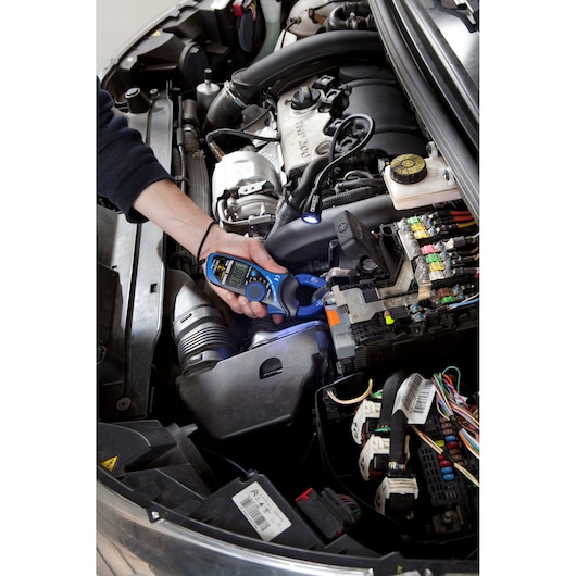 Facom E201803 clamp meter being used to test electrical connections in a car engine bay.