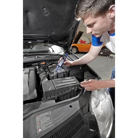 Facom E201804 battery tester used on car battery in garage setting.