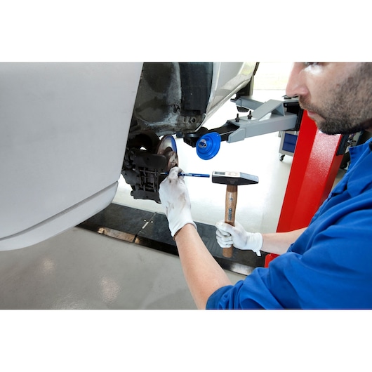 Facom E418226 hammer used by technician in blue uniform working on car brake in workshop setting.