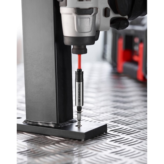 Facom EN_1J24PB screwdriver bit holder in a power drill driving screw into metal bracket, close-up photography.