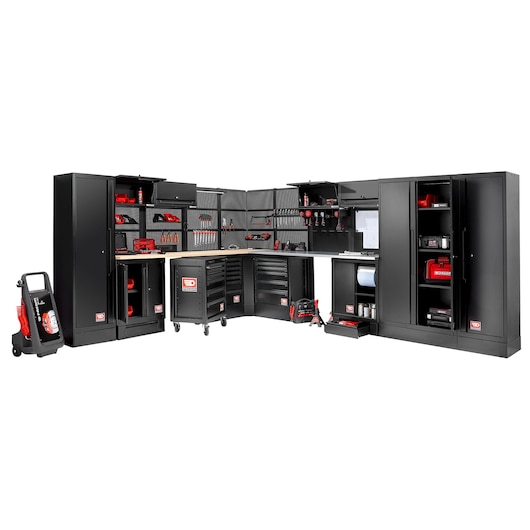 A large modular black tool storage system with multiple cabinets, drawers, and shelves, filled with various red and black tools and accessories. There are work surfaces and pegboards for tool organization. The setup is arranged in an L-shape, suitable for a workshop or garage.