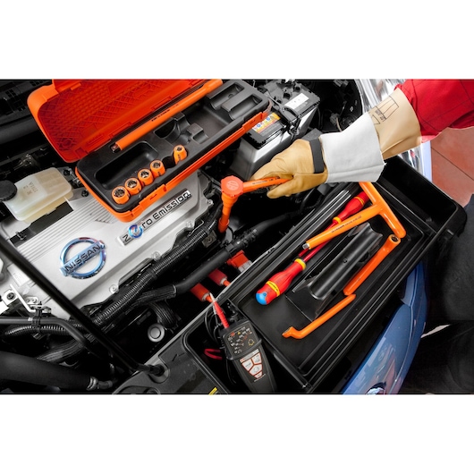 Facom J_151AVSE insulated tool set used on electric car engine, with orange case and various tools visible.