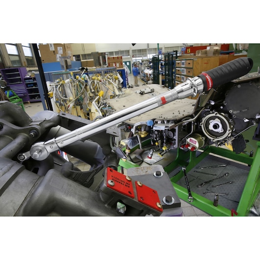Facom J306A100 torque wrench with black grip in use on machinery in an industrial workshop, side angle.
