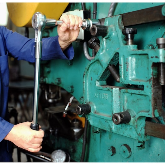 Facom K_151B torque wrench used on industrial machinery by mechanic in blue uniform.