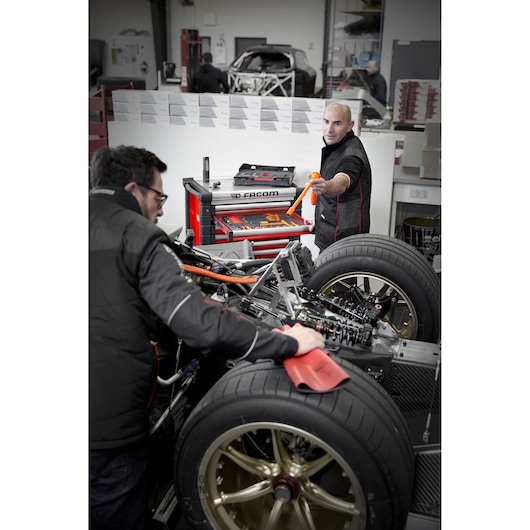 Facom MODM.VSEHYA photography of red tool chest with open drawers beside mechanics working on vehicle chassis.
