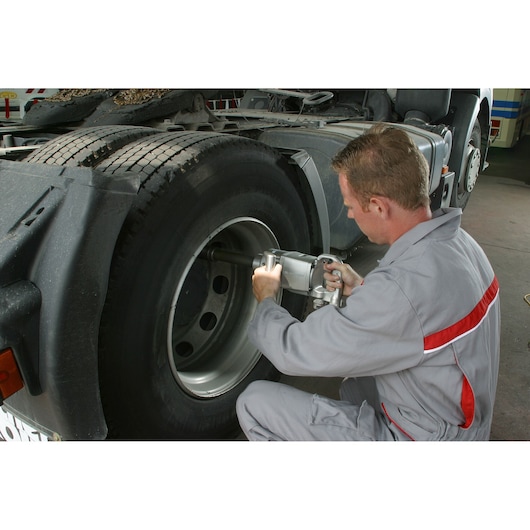 Facom NM_1010LF2 impact wrench used on truck wheel in workshop setting.