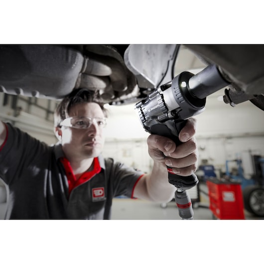 Facom NS.2500GPB impact wrench in use by mechanic under a vehicle in a workshop.