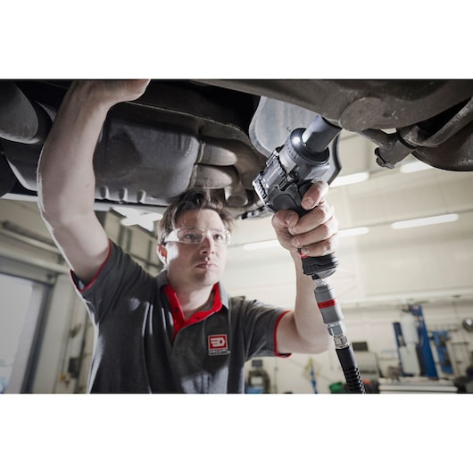 Photo of mechanic using Facom NS2500G impact wrench under a vehicle in a workshop.