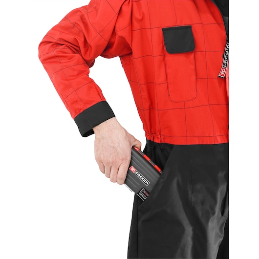 Person wearing a red and black work uniform placing a Facom R.360NANOPB tool case into their pocket.