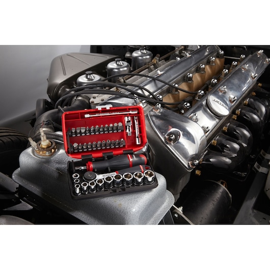 Facom R2NANOPB socket and bit set in red case placed on a car engine, various sockets and bits visible.