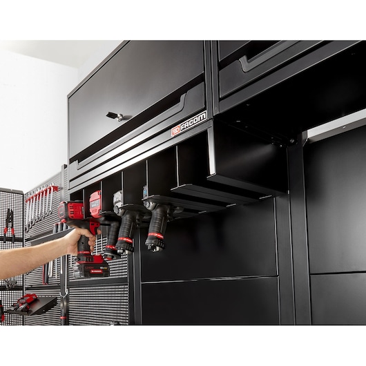 Facom RWS2-POWRACKBS black metal power tool rack mounted under cabinet, four drills stored, photo side angle.