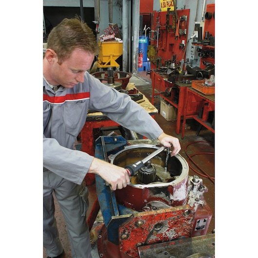 Facom S_215RC torque wrench used by a worker in a workshop for mechanical assembly.