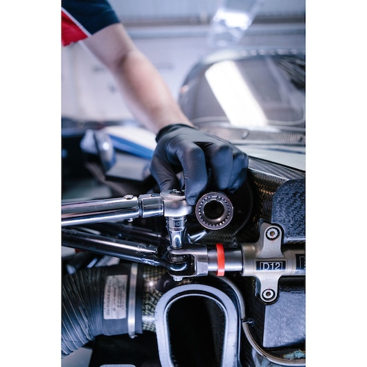 A close-up of a person wearing a black glove and using a Facom ratchet wrench on a mechanical part, likely part of a vehicle engine or machinery.