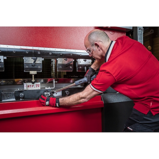 Photo of a worker using Facom S.307A340 torque wrench on industrial metal press wearing red gloves and shirt.