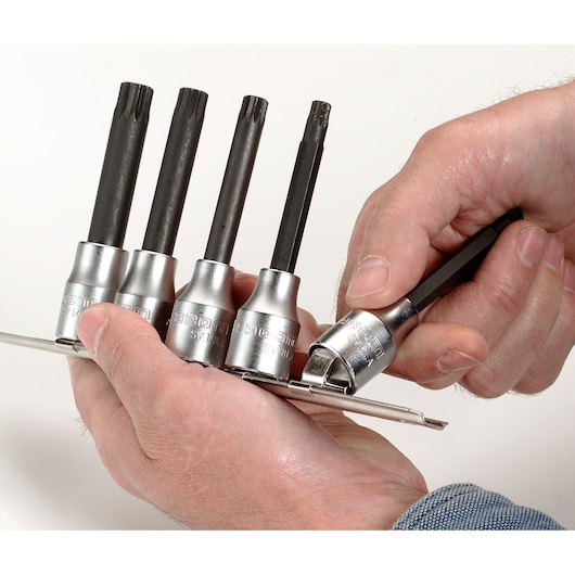 Facom SV_J5 socket bit set held in hand, four black bits with silver sockets on a metal rail, close-up.