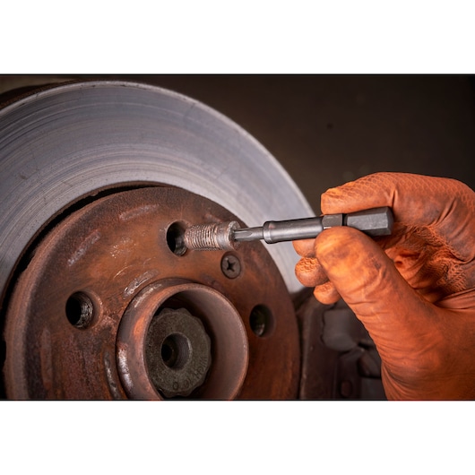 Facom tool SXE_J7MGRPPB used to remove a broken bolt from a rusty brake disc, close-up of gloved hand at work.
