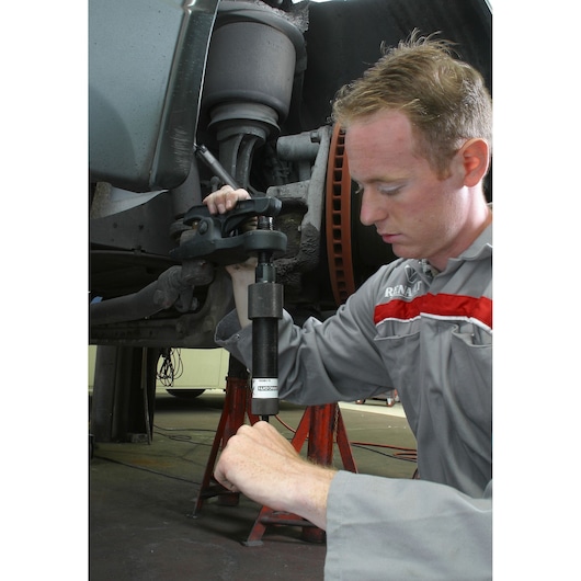 Facom U_18H36 tool used by mechanic on car suspension component, close-up photography.