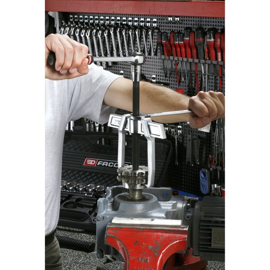 Facom U_232-130 gear puller in use on metal machinery, workshop tools and toolboxes in background.