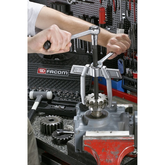 Photo of Facom gear puller in use removing a gear from machinery, SKU U_232-210, workshop tools visible.