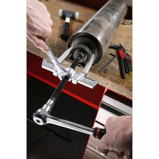 Facom U_232-210 bearing puller tool in use on a workbench, removing bearing from a large metal cylinder.