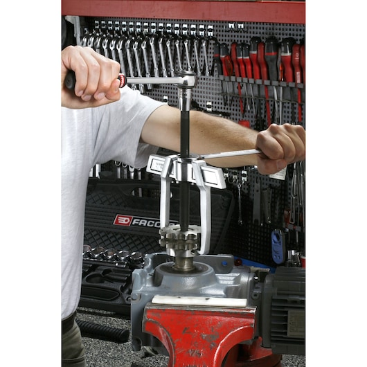 Photo of Facom gear puller in use by technician on metal machinery, SKU U_232-65, workshop tools in background.