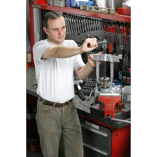 Facom U_232-90 workshop scene with person using hand tools at a workbench, tool storage and red vice visible.