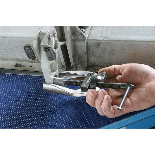 Facom U_301L gear puller tool in use, handheld, applied to metal machinery part.