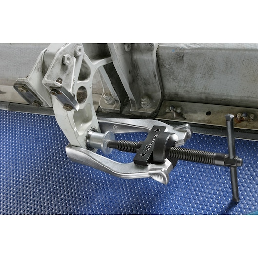 Facom U_301 gear puller tool in use on metal component, close-up view, photography on blue textured surface.