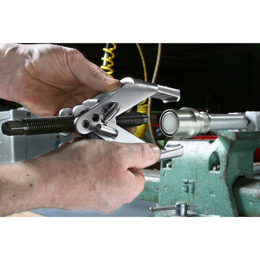 Facom U_35 silver bearing puller tool held by hands, positioned on metal shaft in workshop.