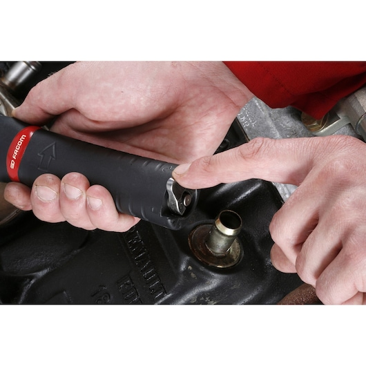 Close-up of a person using a Facom U.48PB tool, showing the hand adjusting its mechanism next to a metallic engine part.