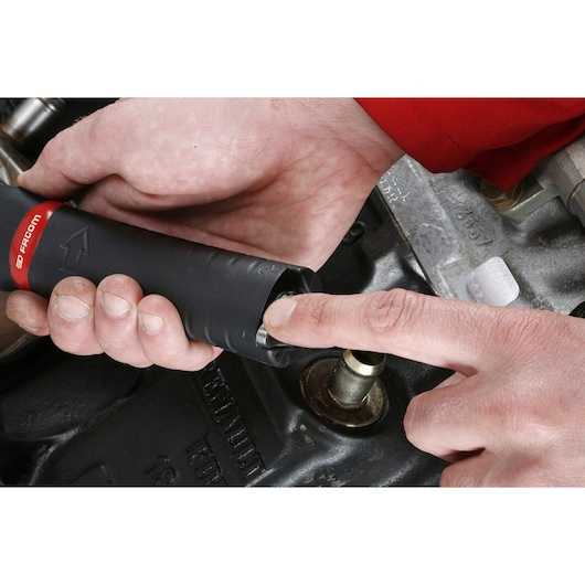 A close-up of a person's hands using a Facom U.48PB tool on a mechanical part, likely an engine component.