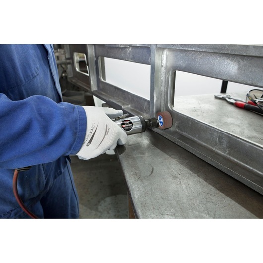 Facom V.345FPB pneumatic grinder in use on metal workpiece, worker wearing gloves and blue coverall.