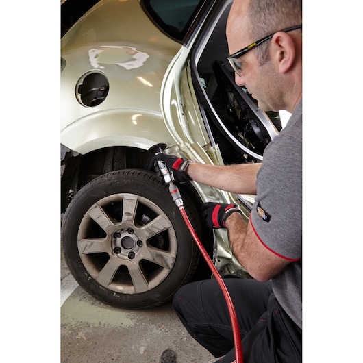 Facom V.345FPB pneumatic tool in use sanding car body near rear wheel, close-up of repair work.