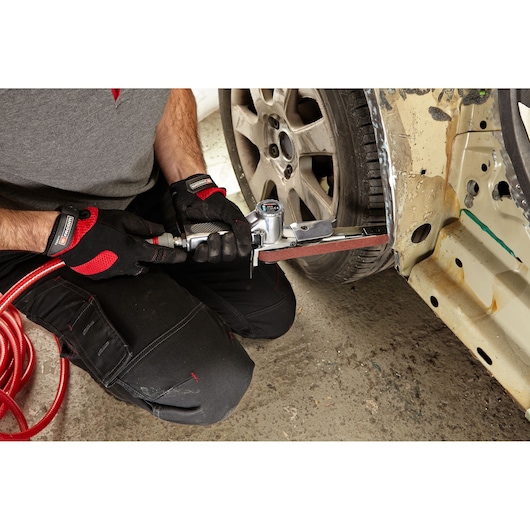 Facom V_403F belt sander used on car body panel, worker wearing black and red gloves.